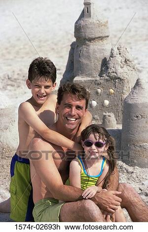 Stock Image - Portrait of a father with his son and daughter sitting on the beach. Fotosearch