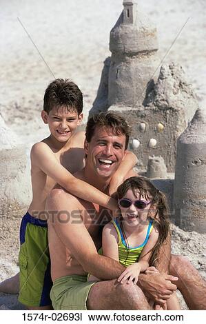 Stock Image - Portrait of a father with his son and daughter sitting on the beach. Fotosearch