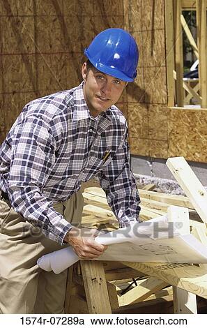 Stock Image - Portrait of a foreman standing at a construction site holding blueprints. Fotosearch