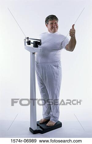 Stock Photo - Portrait of a man standing on a scale showing thumbs up. Fotosearch