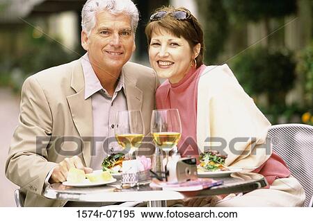 Portrait of a mid adult couple sitting at a table outdoors View Large Photo Image Stock Photography - Portrait of a mid adult couple sitting at a table outdoors. Fotosearch