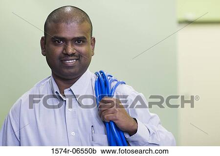 Stock Image - Portrait of a technician carrying computer cables on his shoulder. Fotosearch