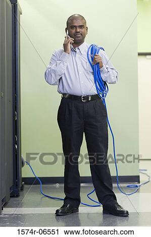 Stock Image - Portrait of a technician carrying computer cables on his shoulder talking on a mobile phone. Fotosearch