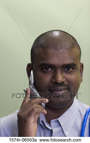 Stock Image - Portrait of a technician carrying computer cables on his shoulder talking on a mobile phone. Fotosearch