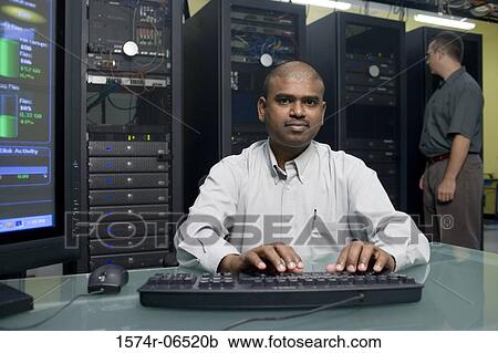 Stock Image - Portrait of a technician using a computer with another technician standing behind him. Fotosearch