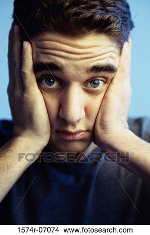 Picture - Portrait of a teenage boy holding the sides of his face. Fotosearch