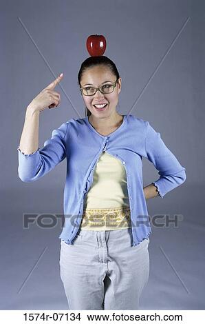 Portrait of a woman standing pointing to an apple on her head View Large Photo Image Picture - Portrait of a woman standing pointing to an apple on her head. Fotosearch