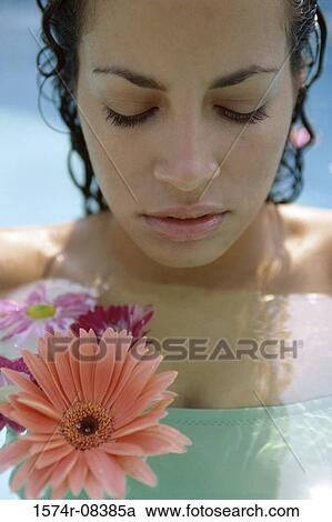 Stock Image - Portrait of a young woman holding a flower looking down. Fotosearch