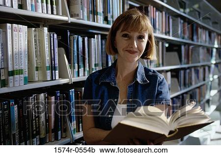 Stock Image - Portrait of a young woman holding books in a library. Fotosearch