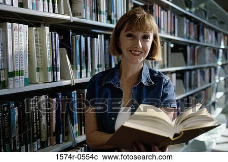 Stock Image - Portrait of a young woman holding books in a library. Fotosearch