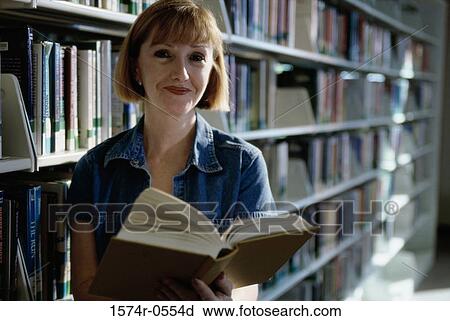 Stock Image - Portrait of a young woman holding books in a library. Fotosearch