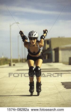 Stock Image - Portrait of a young woman inline skating on road. Fotosearch