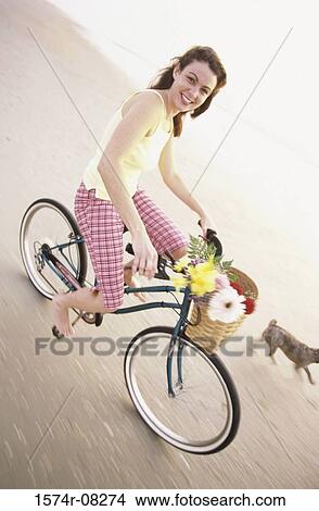 Portrait of a young woman riding a bicycle with her dog running alongside View Large Photo Image Picture - Portrait of a young woman riding a bicycle with her dog running alongside. Fotosearch