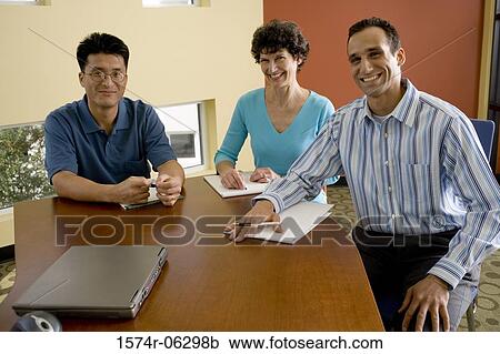 Stock Image - Portrait of two businessmen and a businesswoman sitting in an office. Fotosearch