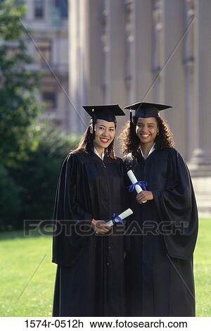 Stock Image - Portrait of two female graduates holding diplomas. Fotosearch