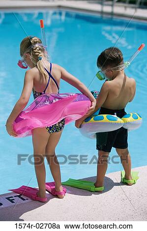 Stock Image - Rear view of a boy and a girl standing at the poolside wearing snorkels and flippers. Fotosearch