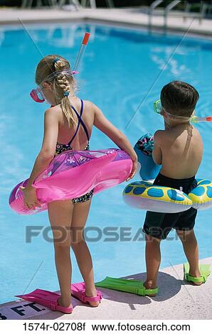 Stock Image - Rear view of a boy and a girl standing at the poolside wearing snorkels and flippers. Fotosearch