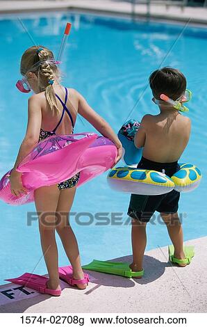 Stock Image - Rear view of a boy and a girl standing at the poolside wearing snorkels and flippers. Fotosearch