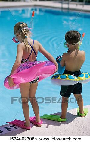 Stock Image - Rear view of a boy and a girl standing at the poolside wearing snorkels and flippers. Fotosearch