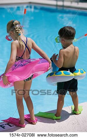 Stock Image - Rear view of a boy and a girl standing at the poolside wearing snorkels and flippers. Fotosearch
