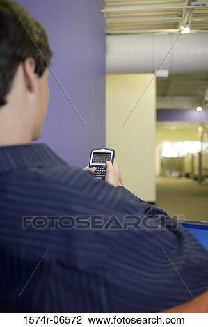Rear view of a businessman holding a hand held device View Large Photo Image Stock Image - Rear view of a businessman holding a hand held device. Fotosearch