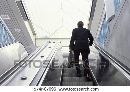 Rear view of a businessman on an escalator View Large Photo Image Stock Photograph - Rear view of a businessman on an escalator. Fotosearch