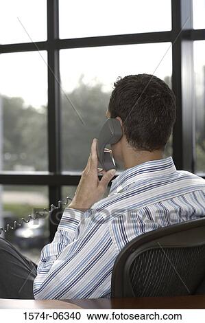Rear view of a businessman using a telephone in an office View Large Photo Image Stock Image - Rear view of a businessman using a telephone in an office. Fotosearch
