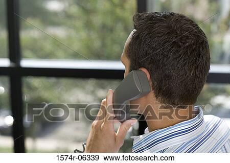 Rear view of a businessman using a telephone in an office View Large Photo Image Stock Photo - Rear view of a businessman using a telephone in an office. Fotosearch