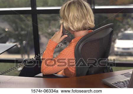 Stock Image - Rear view of a businesswoman talking on a telephone in an office. Fotosearch