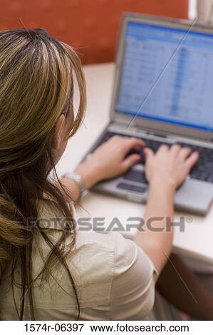 Rear view of a businesswoman working on a laptop in an office View Large Photo Image Stock Photo - Rear view of a businesswoman working on a laptop in an office. Fotosearch