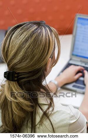 Rear view of a businesswoman working on a laptop in an office View Large Photo Image Stock Photograph - Rear view of a businesswoman working on a laptop in an office. Fotosearch