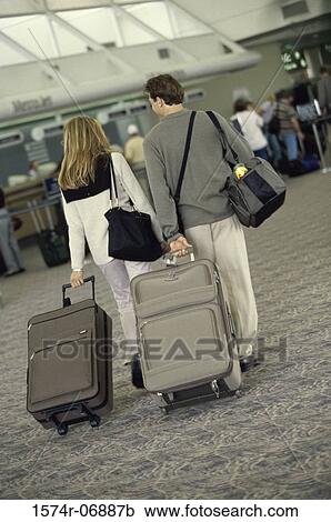 Stock Image - Rear view of a couple walking in an airport. Fotosearch