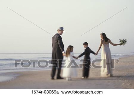 Stock Image - Rear view of a newlywed couple walking on the beach with a bridesmaid and a ring bearer. Fotosearch