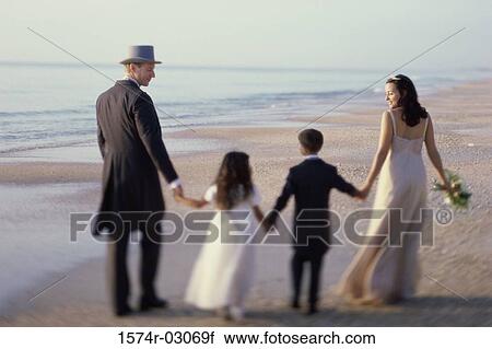 Stock Image - Rear view of a newlywed couple walking on the beach with a flower girl and a ring bearer. Fotosearch