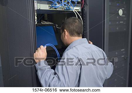Stock Photograph - Rear view of a technician looking at a computer monitor in a server room. Fotosearch