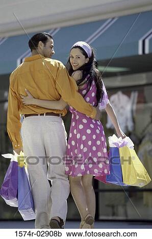 Stock Image - Rear view of a young couple walking with shopping bags. Fotosearch