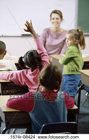 Picture - School children raising their hands in class. Fotosearch