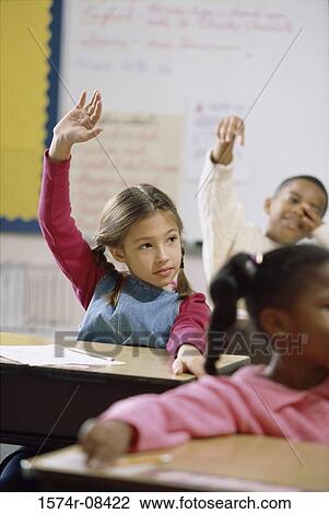Stock Image - School children raising their hands in class. Fotosearch