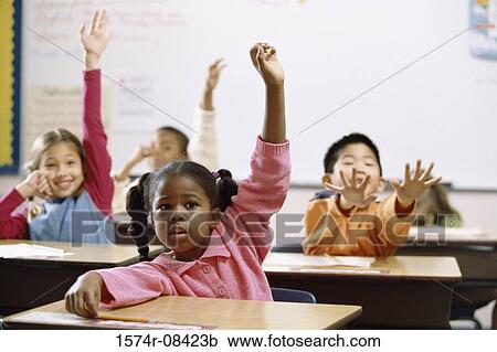 Stock Image - School children raising their hands in class. Fotosearch