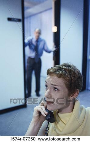 Secretary talking on a telephone with a businessman standing in a doorway behind View Large Photo Image Stock Image - Secretary talking on a telephone with a businessman standing in a doorway behind. Fotosearch