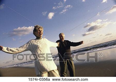 Stock Image - Senior couple holding hands at the beach. Fotosearch