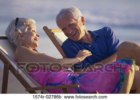 Stock Image - Senior couple sitting in deck chairs on the beach. Fotosearch