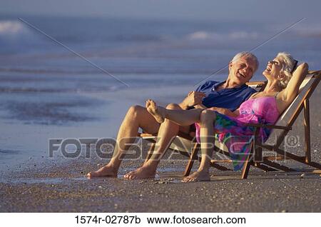 Stock Image - Senior couple sitting in deck chairs on the beach. Fotosearch
