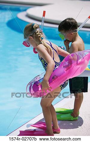 Stock Image - Side profile of a boy and a girl standing at the poolside wearing snorkels and flippers. Fotosearch
