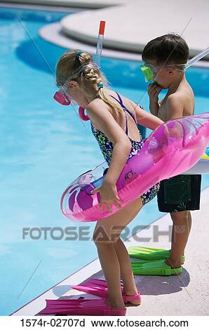 Stock Image - Side profile of a boy and a girl standing at the poolside wearing snorkels and flippers. Fotosearch