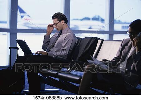 Stock Image - Side profile of a businessman and a businesswoman sitting in an airport lounge. Fotosearch