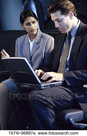 Stock Image - Side profile of a businessman and businesswoman sitting in front of a laptop. Fotosearch