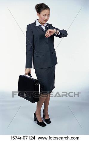 Picture - Side profile of a businesswoman looking at her wristwatch holding a briefcase. Fotosearch