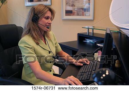 Stock Image - Side profile of a businesswoman wearing a headset working on a computer. Fotosearch