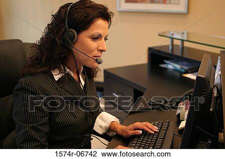 Stock Image - Side profile of a businesswoman wearing a headset working on a computer. Fotosearch